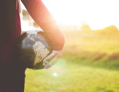 person holding black and brown globe ball while standing on grass land golden hour photography